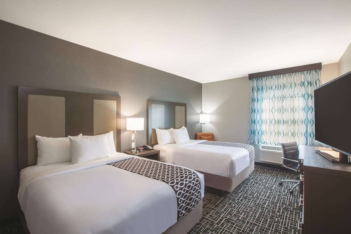 A hotel room with two beds, a desk, a chair, a TV, and a window with curtains.