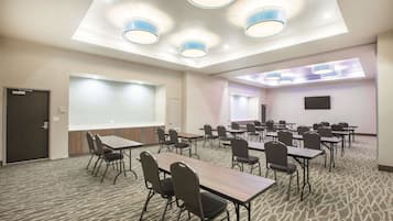 Un salón de conferencias con mesas y sillas, una pantalla de proyector y un ventanal grande.