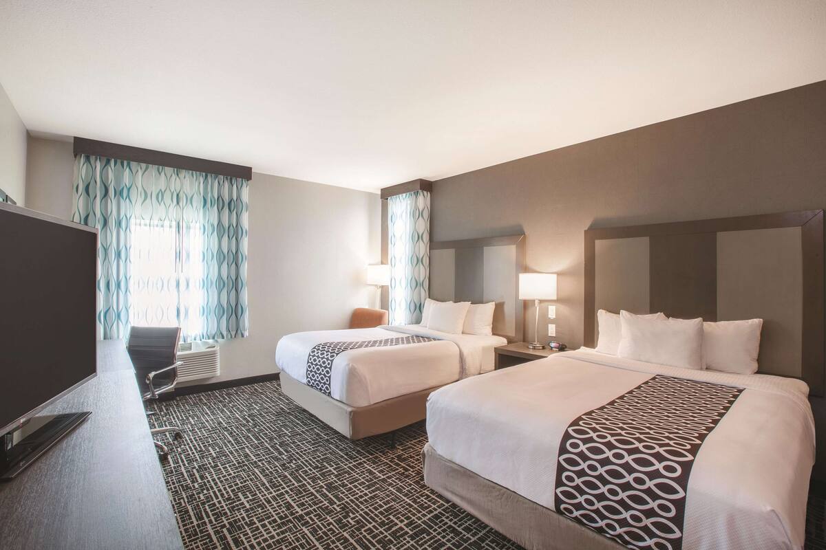 A hotel room with two beds, a desk, a TV, and a patterned carpet.