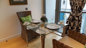 A dining area with wicker furniture, a glass table, and a view of the street through a window.