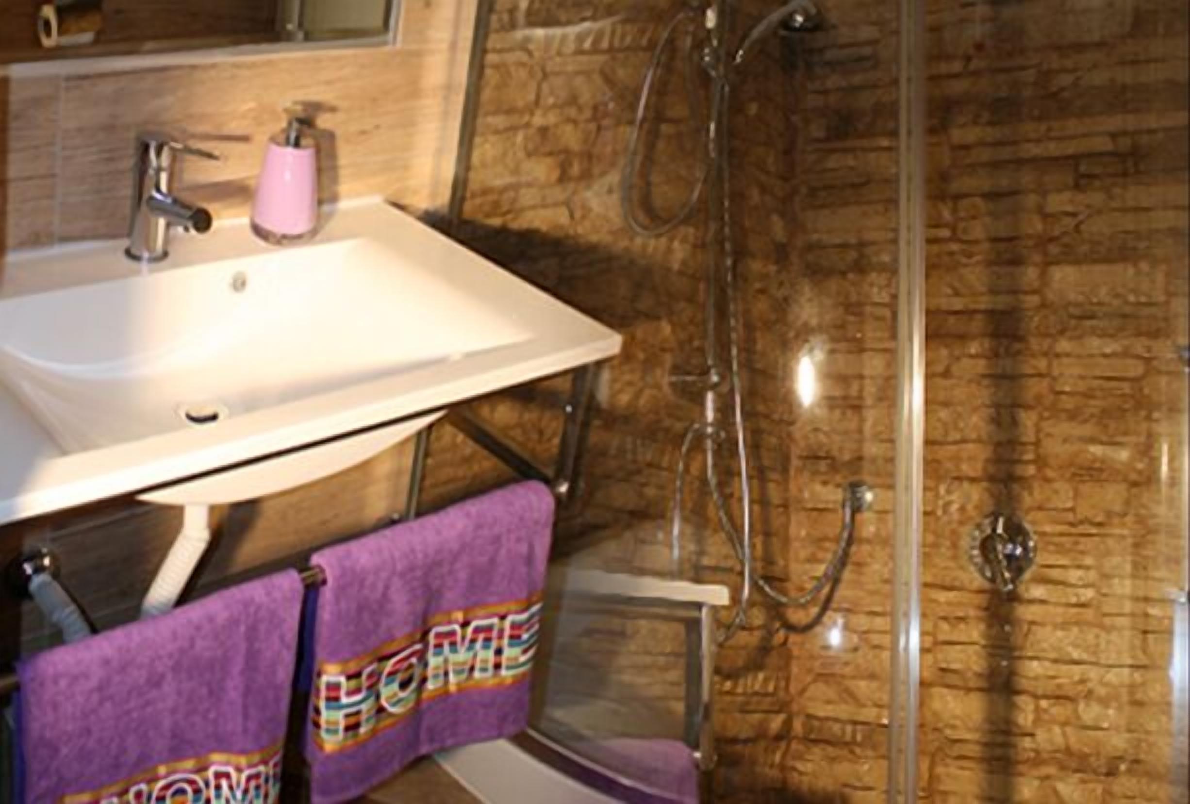 A bathroom with a white sink, a pink soap dispenser, and a shower with a glass door.