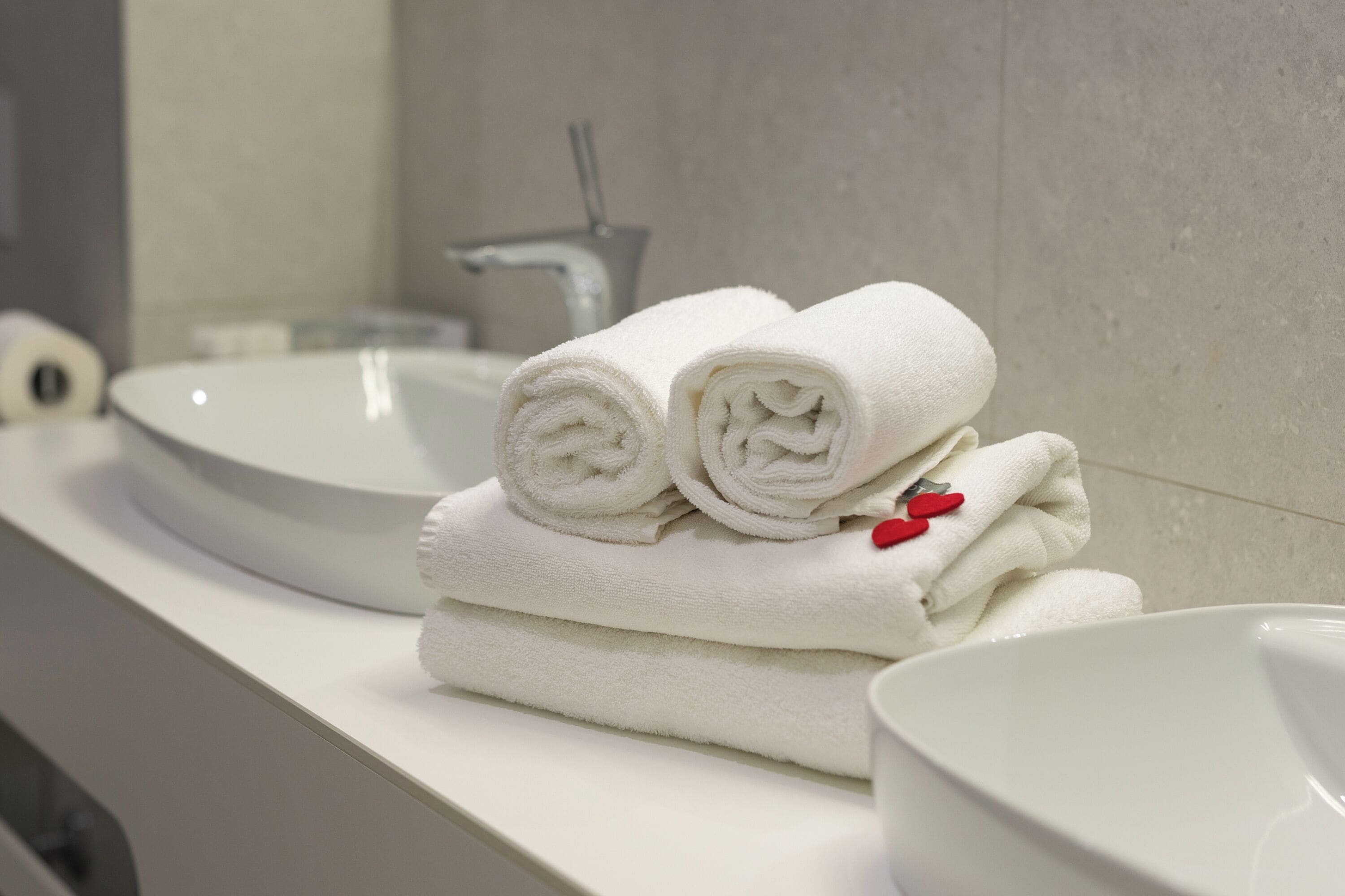 A bathroom with a white sink, a mirror, and a towel stack with red heart decorations.
