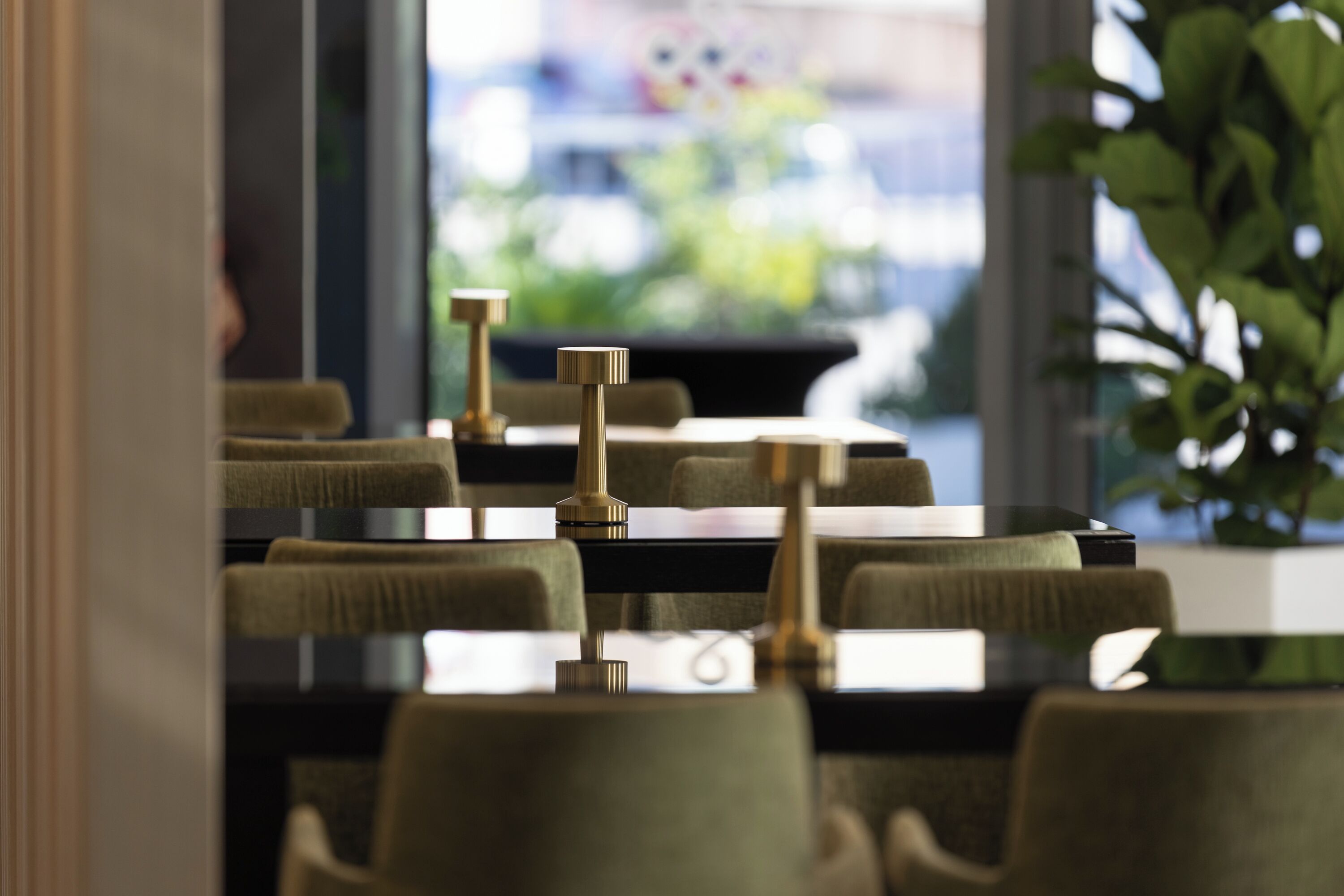Un restaurant au décor moderne, avec une longue table entourée de chaises et un luminaire décoratif en laiton.