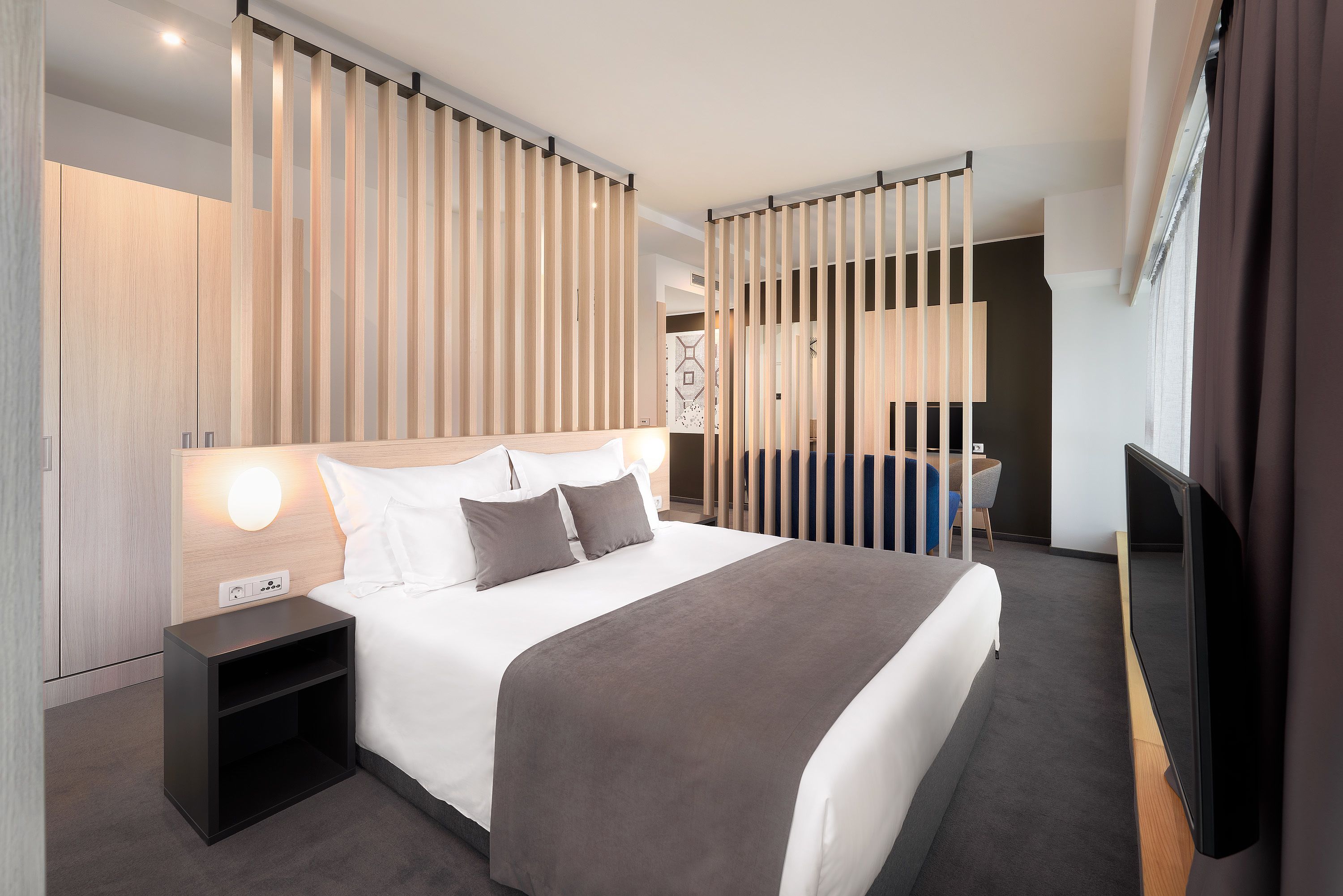 Habitación de hotel moderna con una cama grande, mesitas de noche, televisor y vistas a la ciudad.