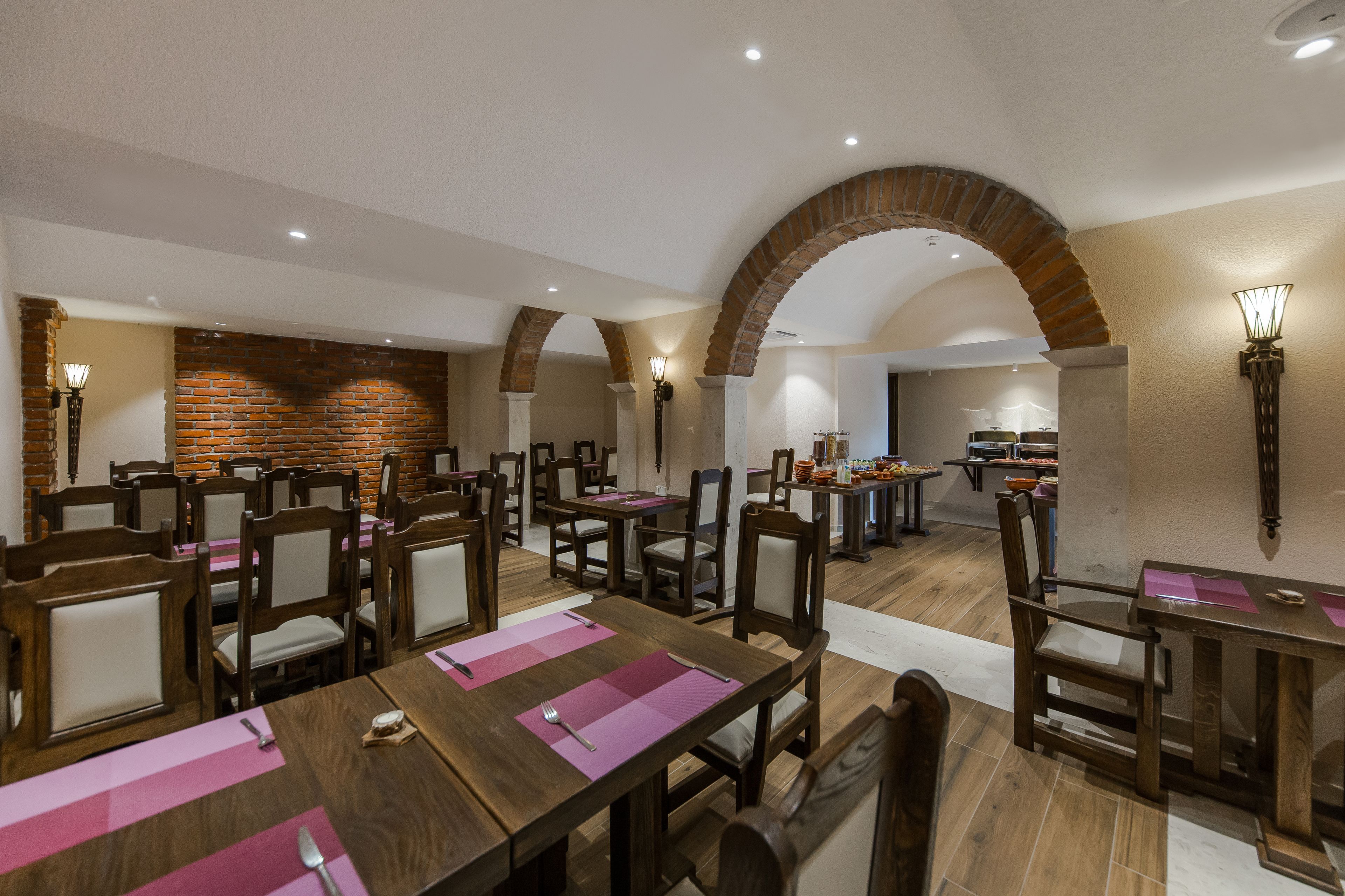 A dining area with wooden tables and chairs, brick walls, and a brick archway.