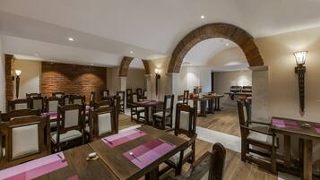 A dining area with wooden tables and chairs, brick walls, and a brick archway.