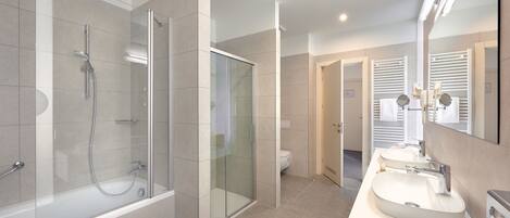 Un baño moderno con ducha envuelta en vidrio, una bañera y un lavamanos con dos lavabos y un espejo.