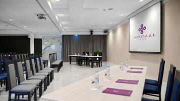 A conference room with a long table, chairs, and a screen displaying the hotel name.