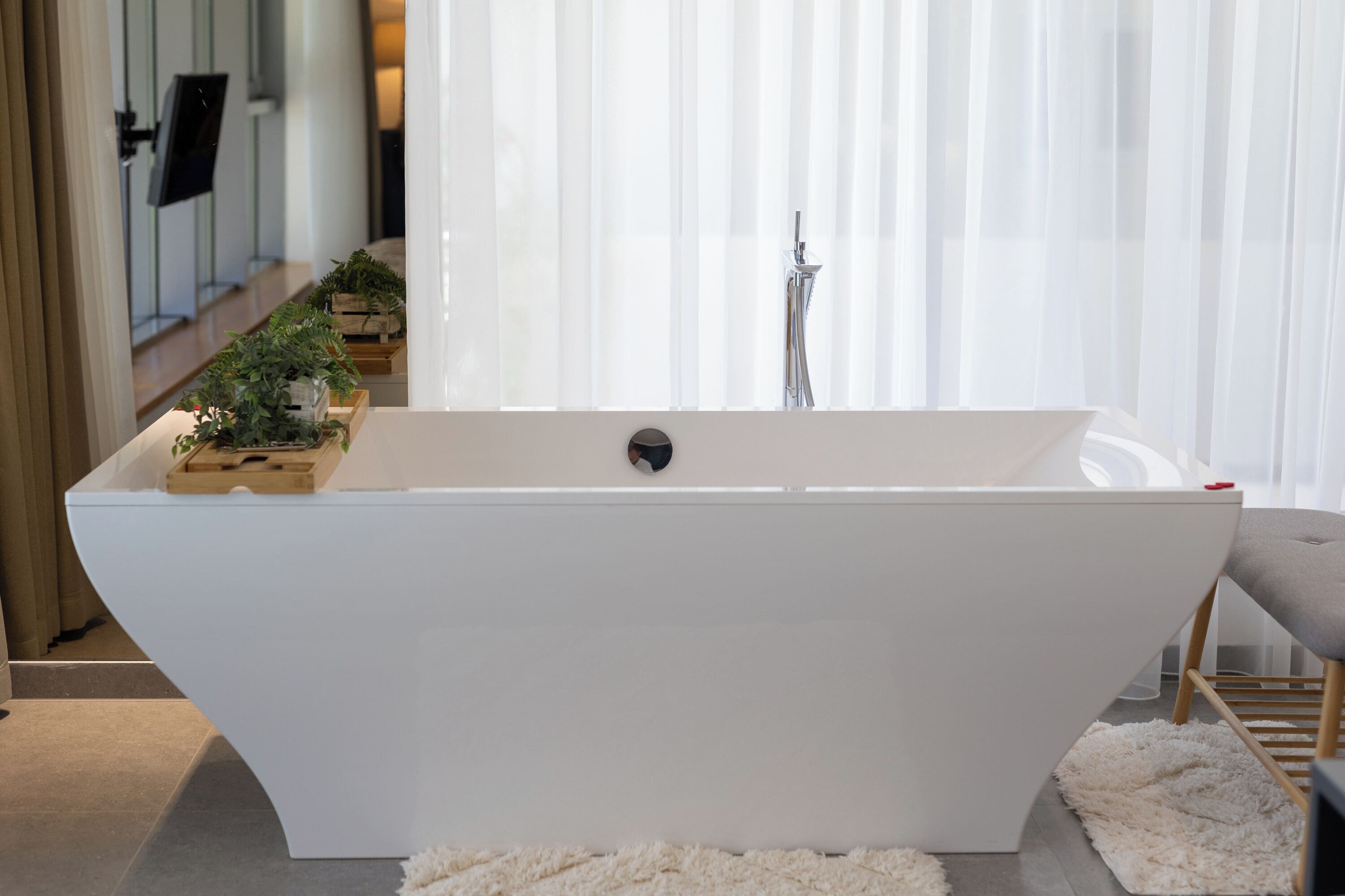 A modern bathroom with a freestanding bathtub, a wooden side table with plants, and a fluffy white rug.