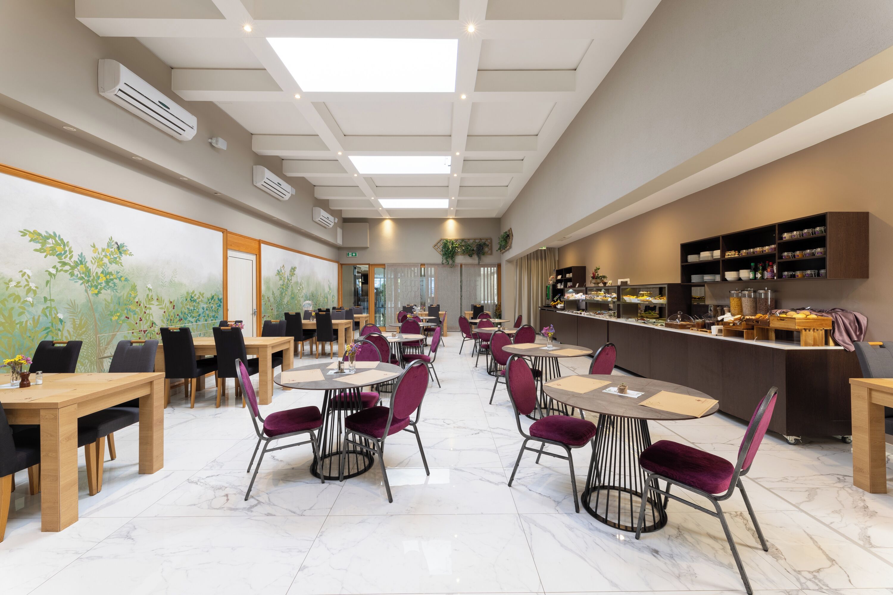 A spacious dining area with multiple tables and chairs, a counter with food items, and a mural on the wall.