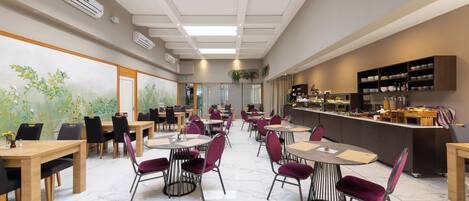 A spacious dining area with multiple tables and chairs, a counter with food items, and a mural on the wall.