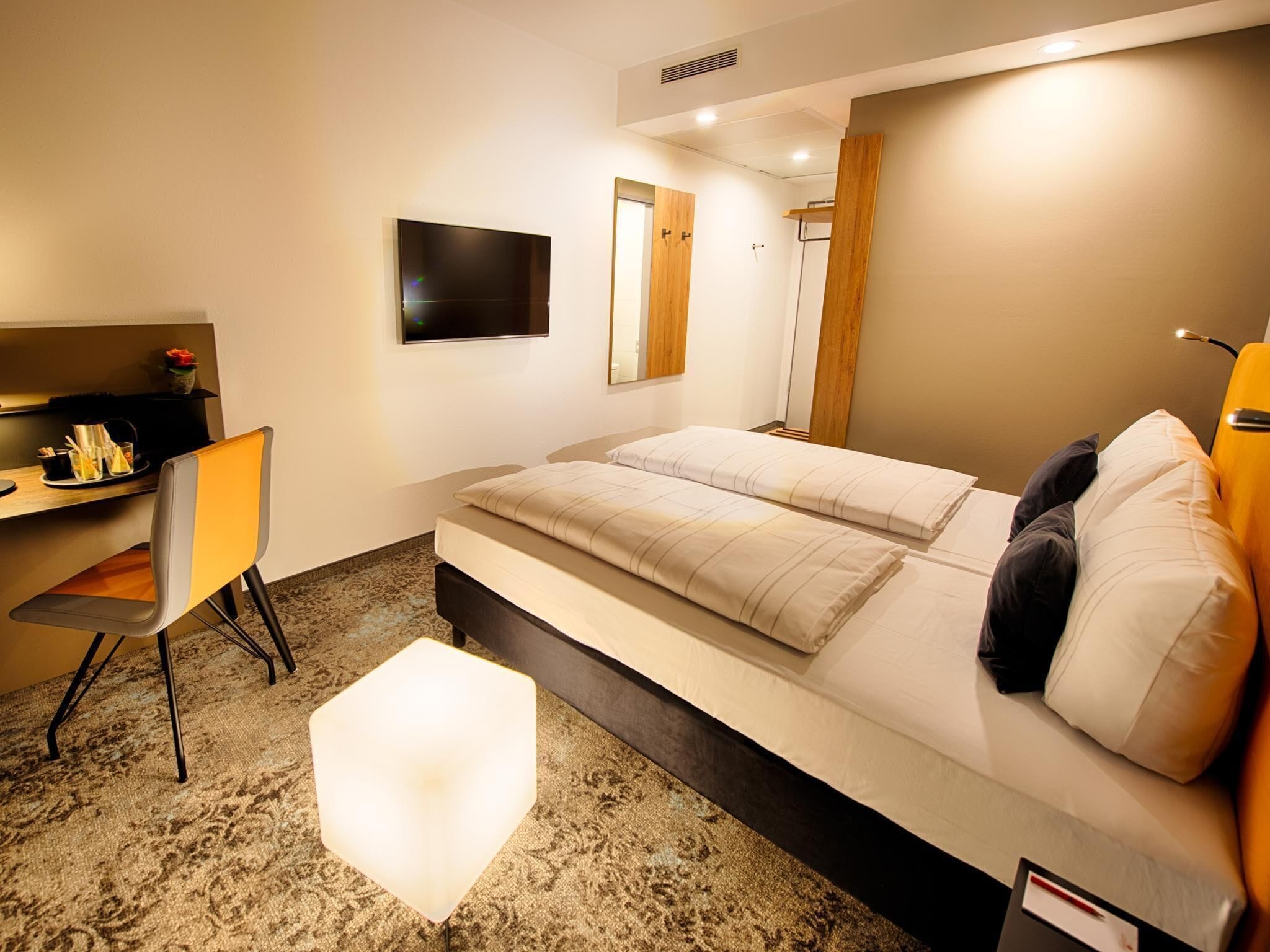 A modern hotel room with a bed, a desk, a chair, and a TV.
