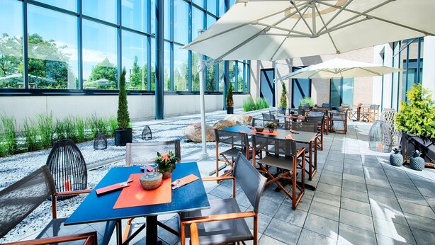 An outdoor patio area with tables and chairs, large umbrellas, and potted plants.