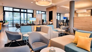 A modern lounge area with seating arrangements, a coffee table, and a large window providing a view of the outdoors.