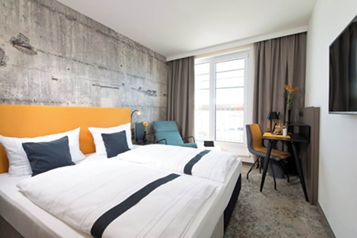 Habitación de hotel con una cama grande, un escritorio con silla, televisor y vistas al exterior.
