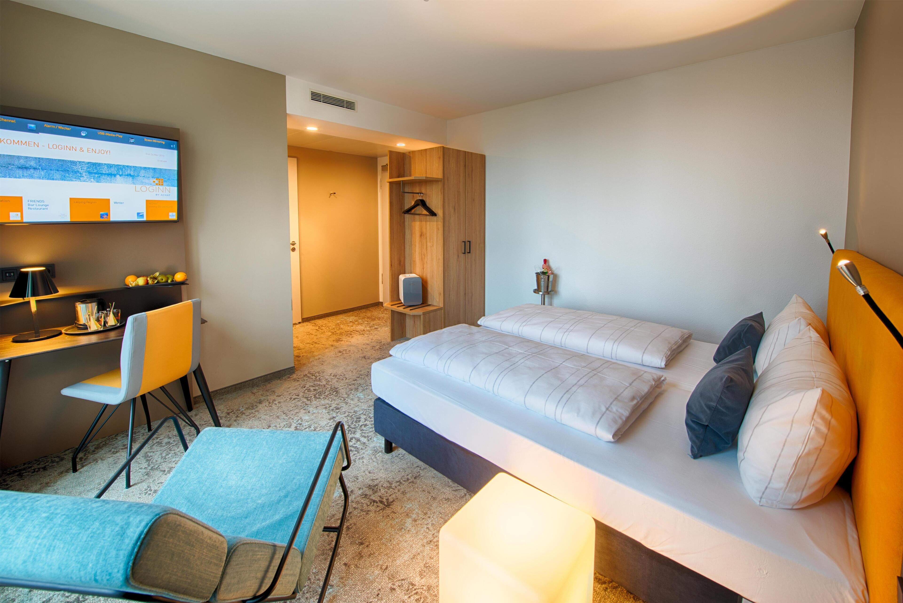 Ein modernes Hotelzimmer mit Bett, Schreibtisch, Sessel und Fernseher, der einen Anmeldebildschirm zeigt.