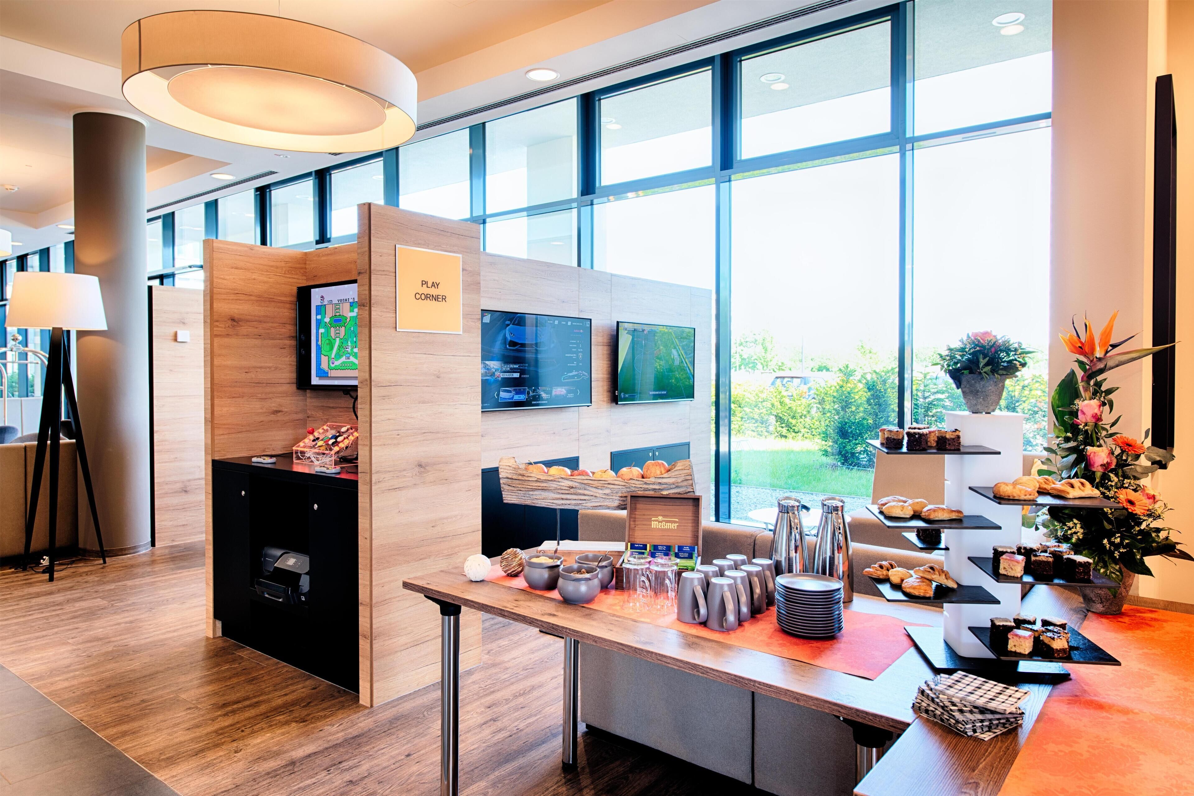 A modern hotel lobby with a reception desk, a play corner, and a buffet area with various food items.