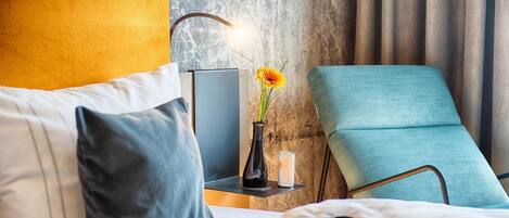A neatly arranged hotel room with a bed, a bedside table with a lamp, a vase with a flower, and a chair.