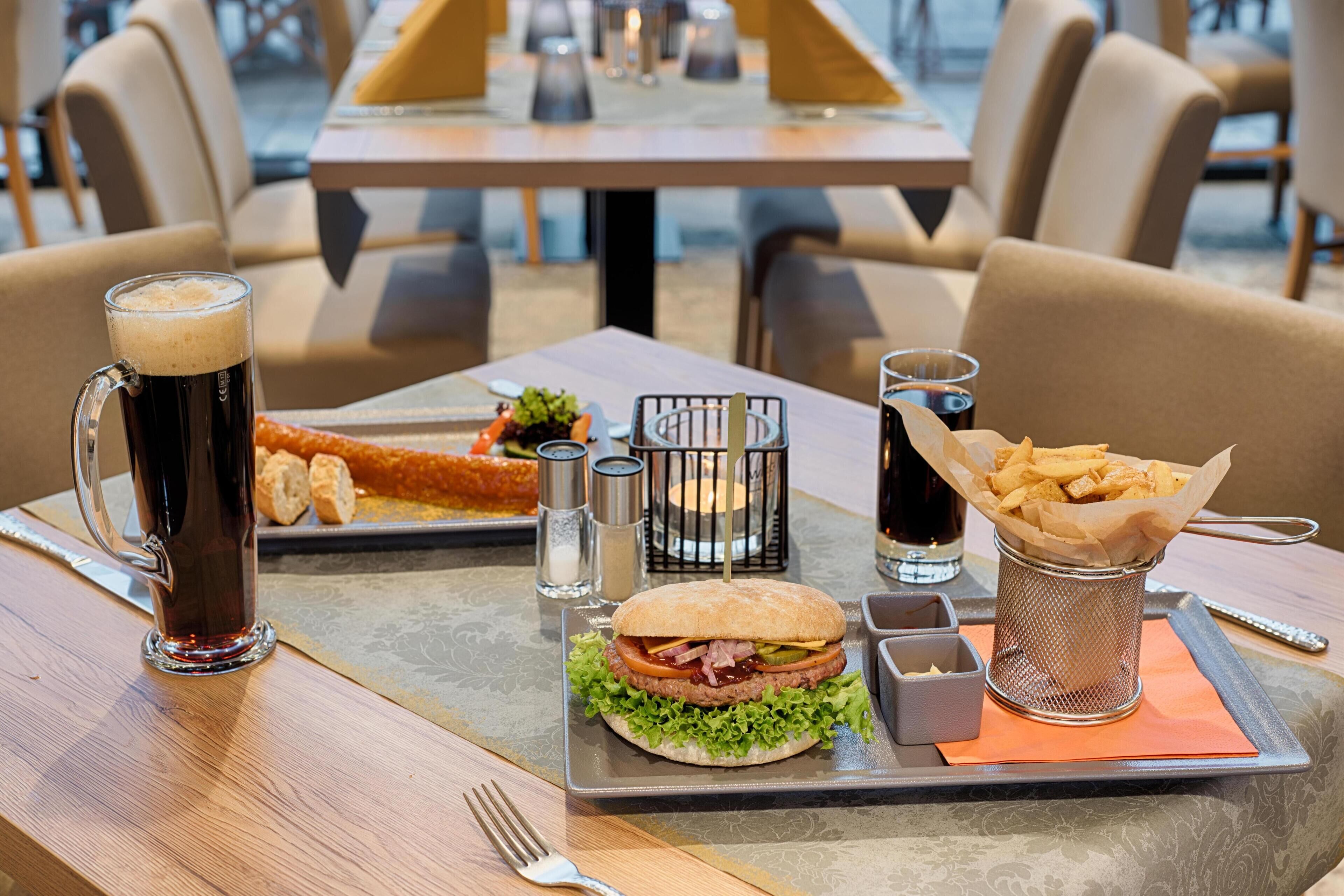 Une table à manger avec un hamburger, des frites, un pichet de bière et des condiments.