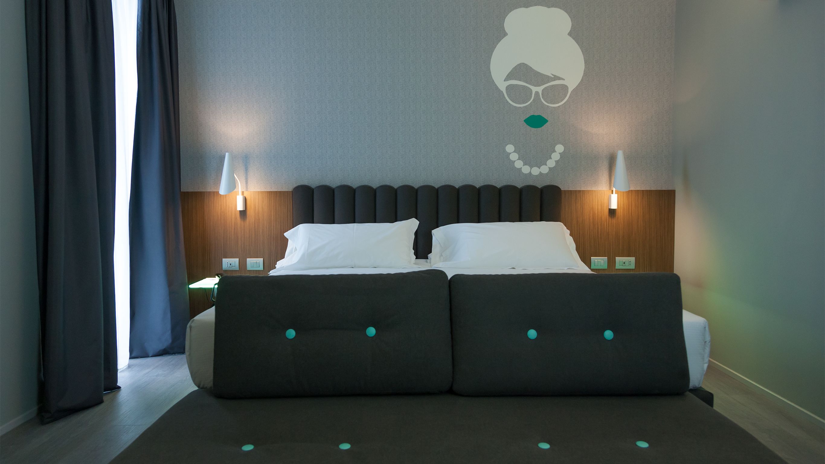 Moderni hotellihuone, jossa on suuri sänky, kaksi yöpöytävalaisinta ja seinälle kiinnitetty taideteos.