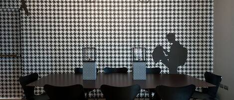 Une salle de conférence avec un mur orné d’un motif à carreaux, une table ronde et six chaises.