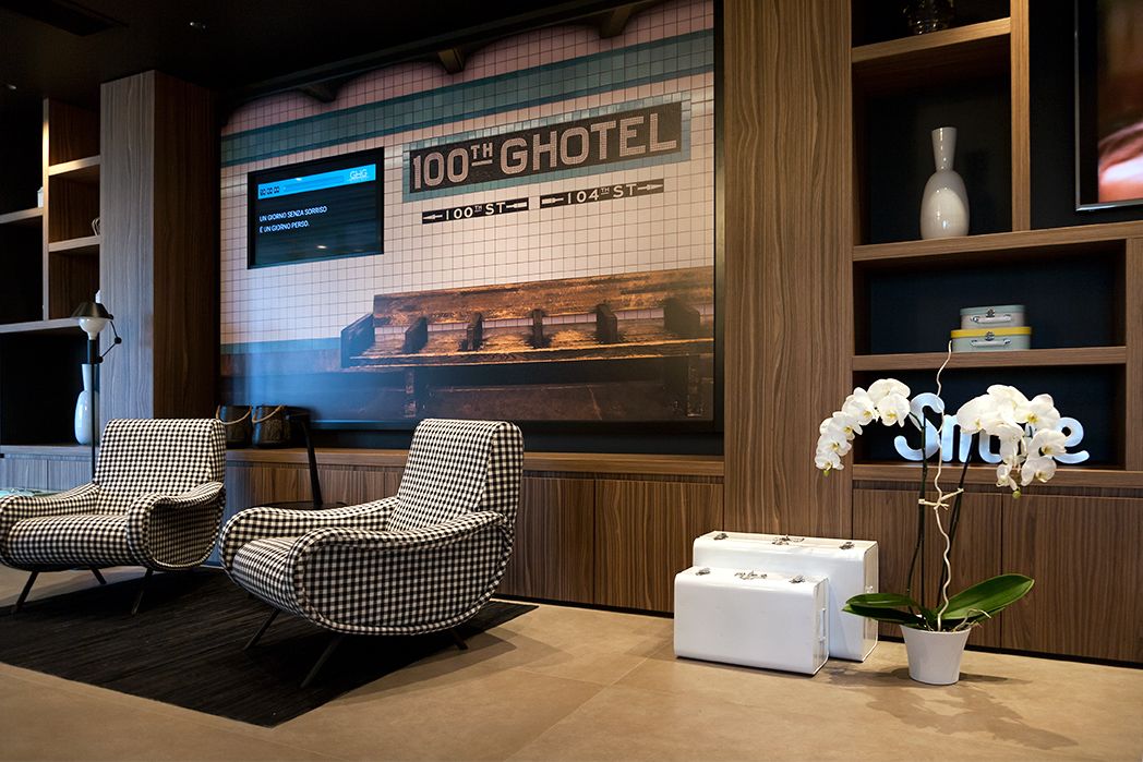 Eine Lobby mit karierten Sesseln, einem großen digitalen Bildschirm und einer Topfpflanze mit Orchideen.
