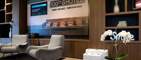 A lobby with checkered armchairs, a large digital display, and a potted orchid.