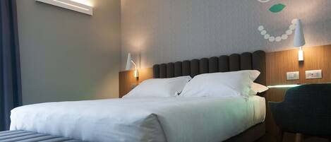 A hotel room with a bed, bedside lamps, a wall clock, and a chair.