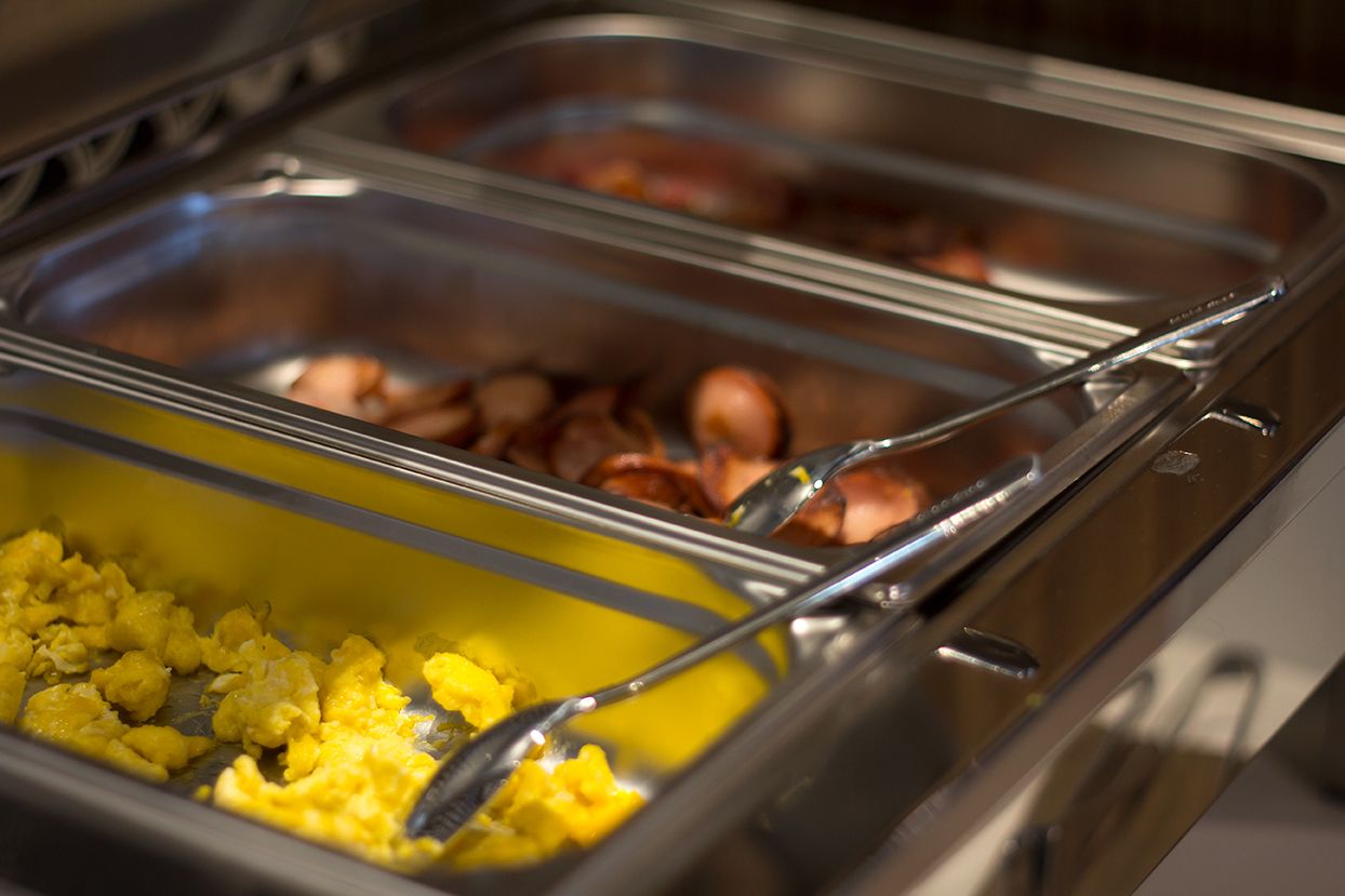 A buffet with various food options including scrambled eggs, bacon, and sausages.