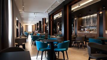 A modern restaurant with round tables and blue chairs, featuring a bar area with a wooden counter and pendant lighting.