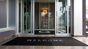 A modern hotel entrance with a glass door, a welcome mat, and a chandelier. - G Hotel Pescara (Pescara)