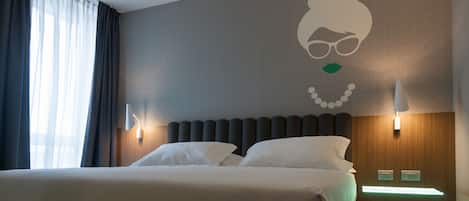 Ein Hotelzimmer mit einem großen Bett, zwei Nachttischlampen, einer Wandleuchte und einem Fenster mit Vorhängen.