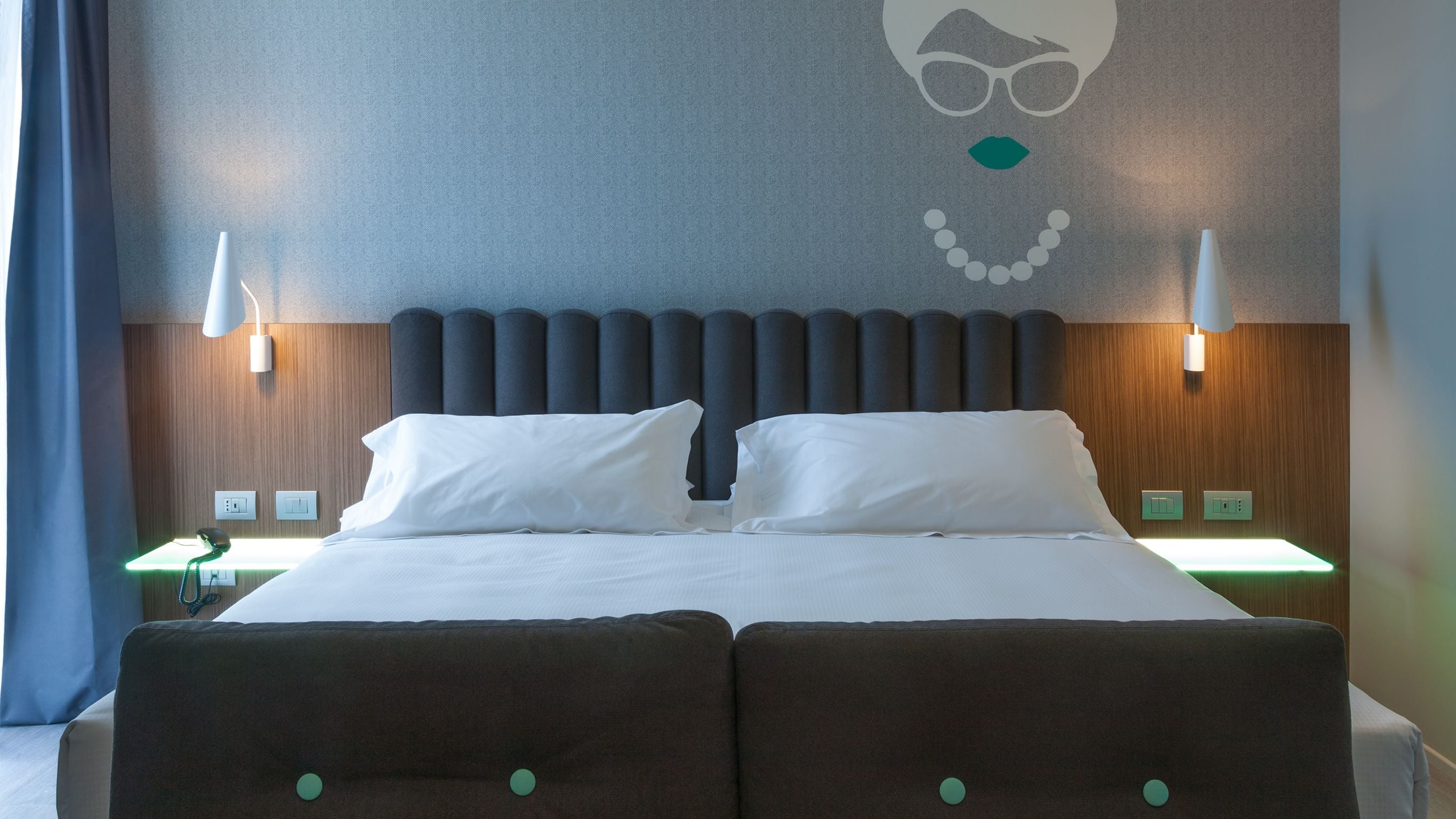 A double bed with white linens, a grey headboard, and two bedside lamps.