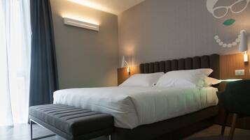 A neatly made bed with white linens, a grey bench, and a wall-mounted lamp.