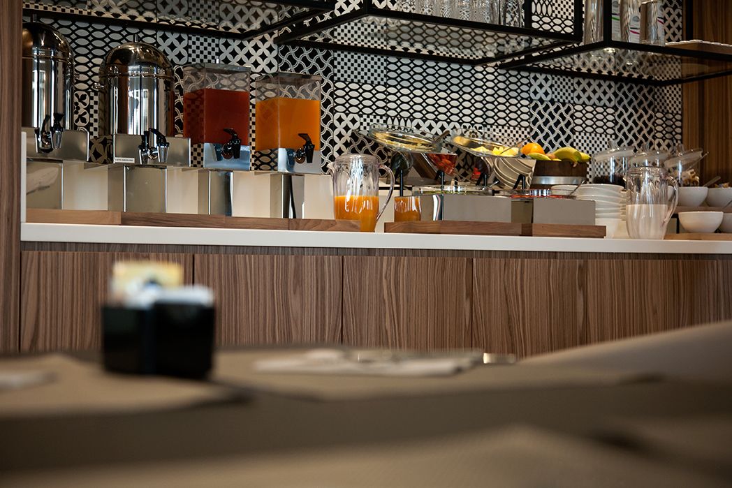 A breakfast bar with a variety of food and drink options, including fruits, a pitcher of orange juice, and a coffee machine.