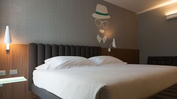 Una cama bien tendida con sábanas blancas, cabecera con ranuras verticales y una lámpara de pared.