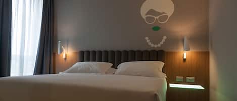 A hotel room with a large bed, two bedside tables, a wall-mounted light fixture, and a decorative wall art piece.