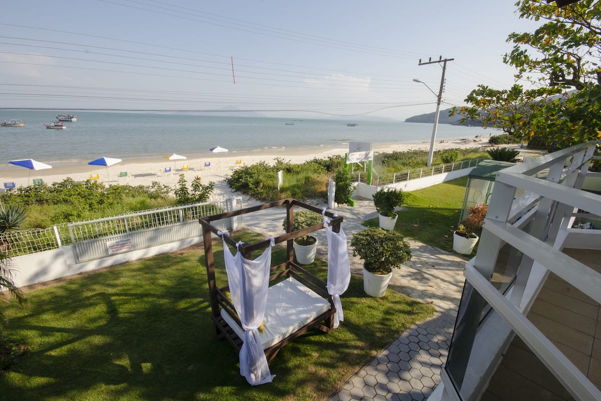 A balcony with a view of the beach, a white fence, and potted plants.