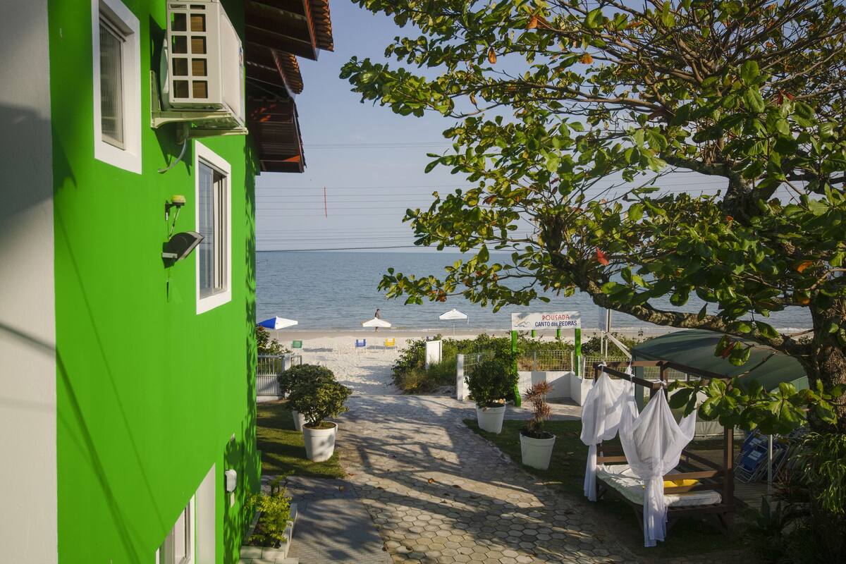 A green building with a view of the sea, outdoor seating, and potted plants.