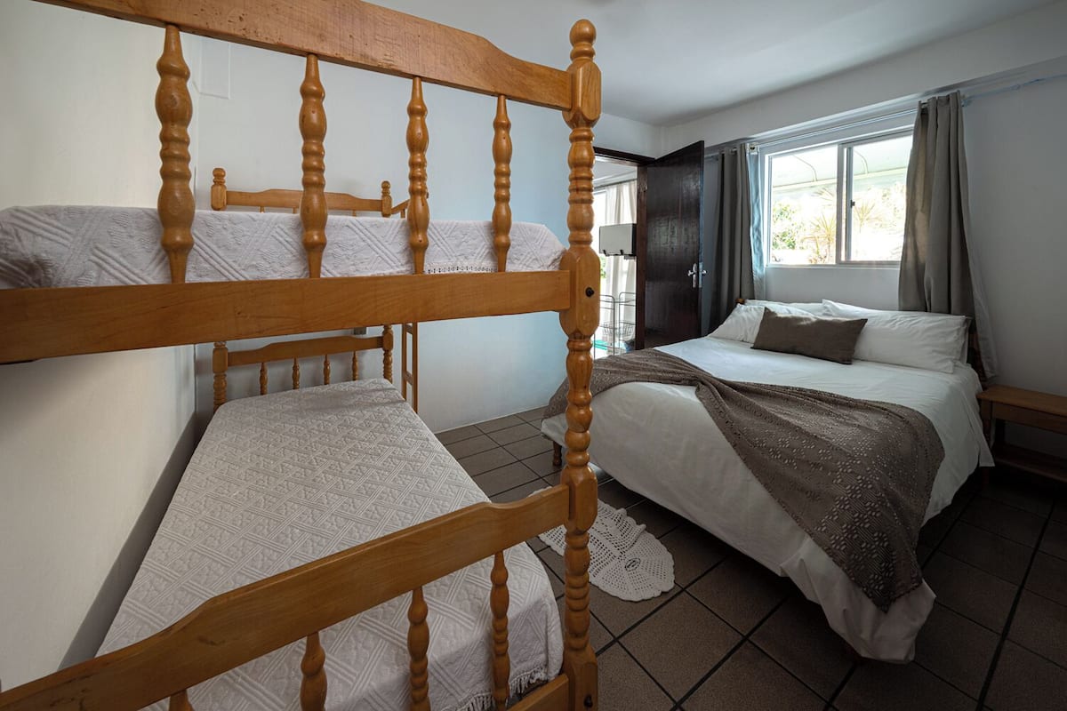A room with two wooden bunk beds, a single bed, and a window with curtains.