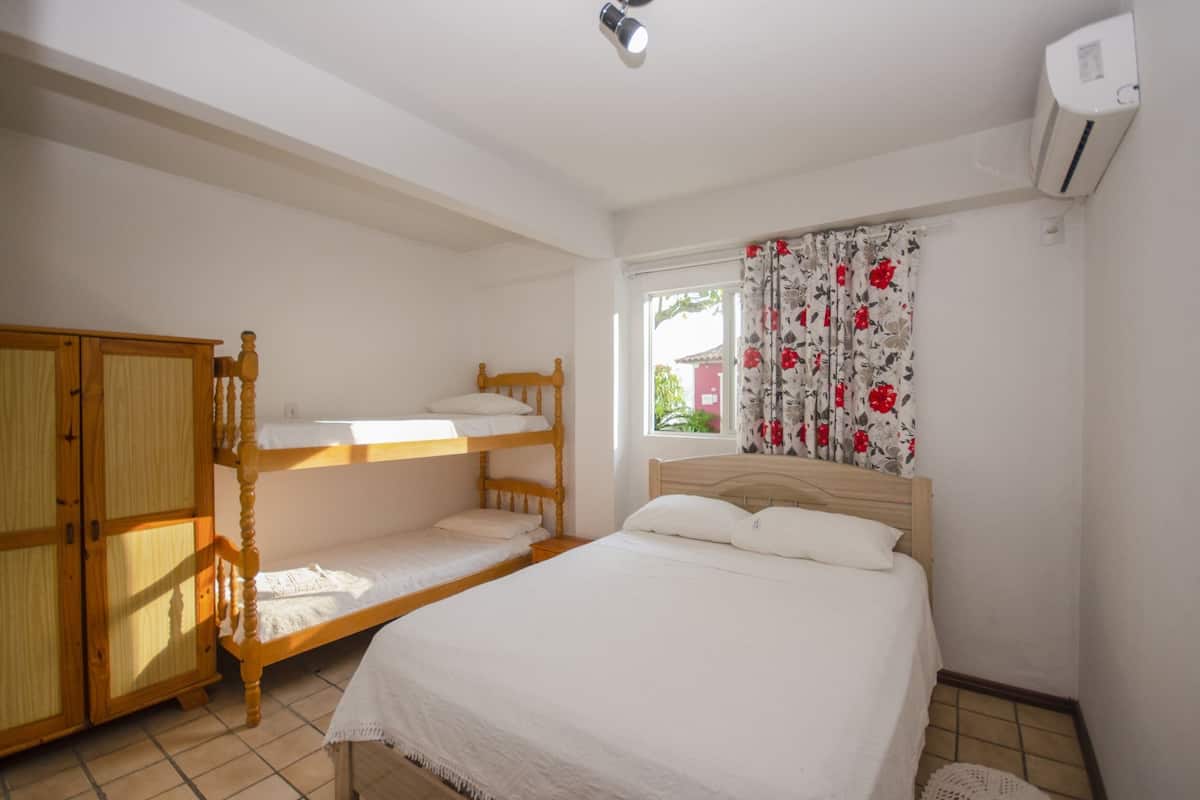 A bedroom with bunk beds, a wooden wardrobe, a bed with white bedding, and a window with floral curtains.