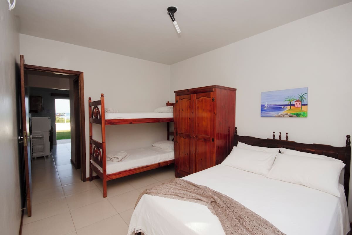 A room with bunk beds, a wooden wardrobe, a painting of a beach scene, and a door leading to a balcony.