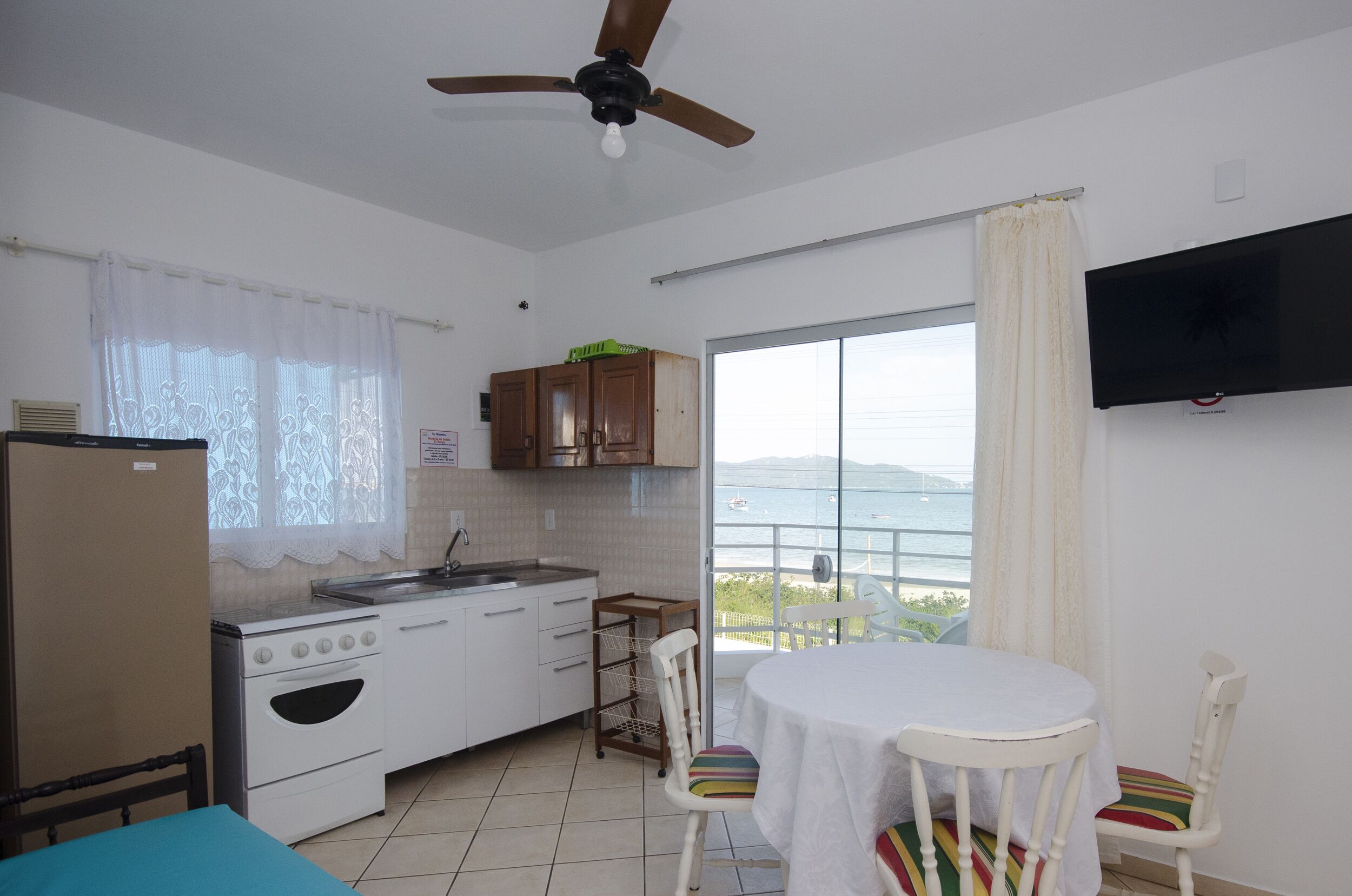 Una cocina compacta con estufa, lavabo y armarios, un comedor con mesa y sillas, y un balcón con vista al mar.