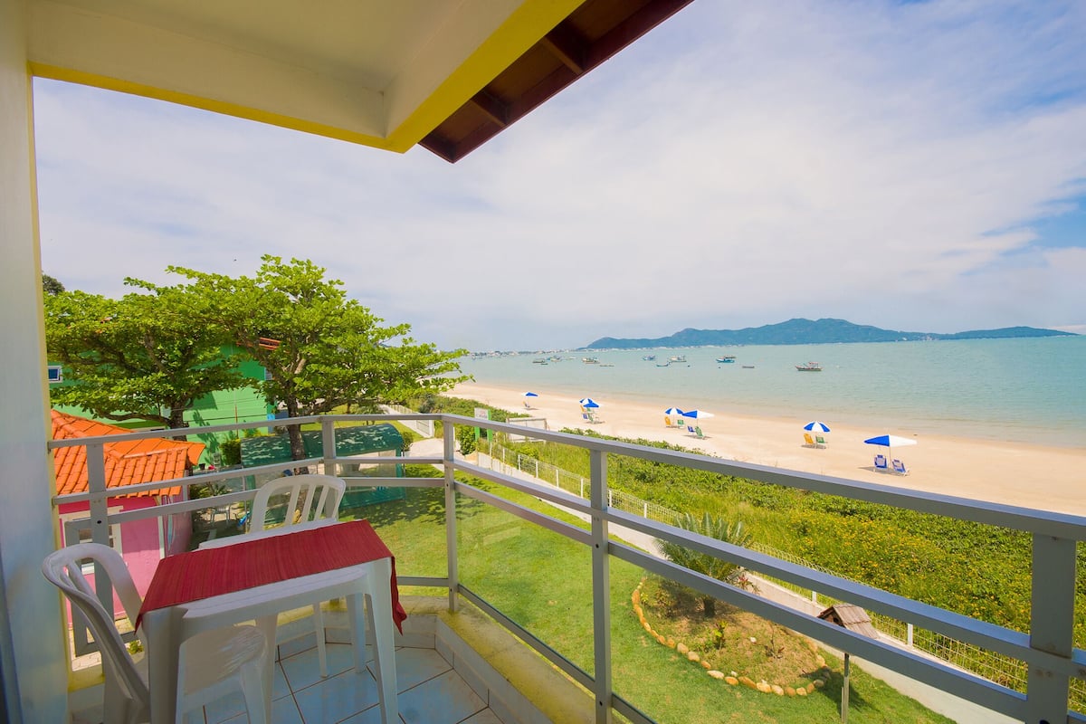 A balcony with a table and chairs, overlooking a beach with boats and umbrellas.