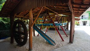 Un parque infantil con tobogán y columpios bajo una estructura de madera.