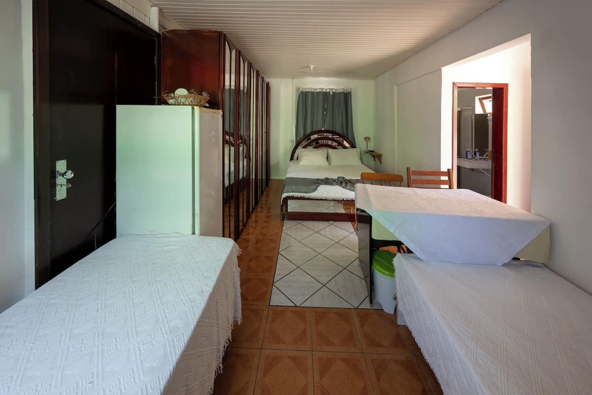 A narrow room with a bed, a small table, and a refrigerator.