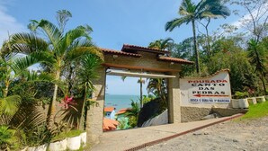 Un arco de piedra que conduce a una vista costera, con un cartel que dice 'Pousada Cantos das Pedras' y la fecha 'Desca e Suba na 1ª Marcha'.