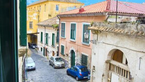 A narrow street with buildings on either side, a blue car parked on the right, and a yellow building in the background. - Elegant B&B Il Vicolo storico (Salerno)