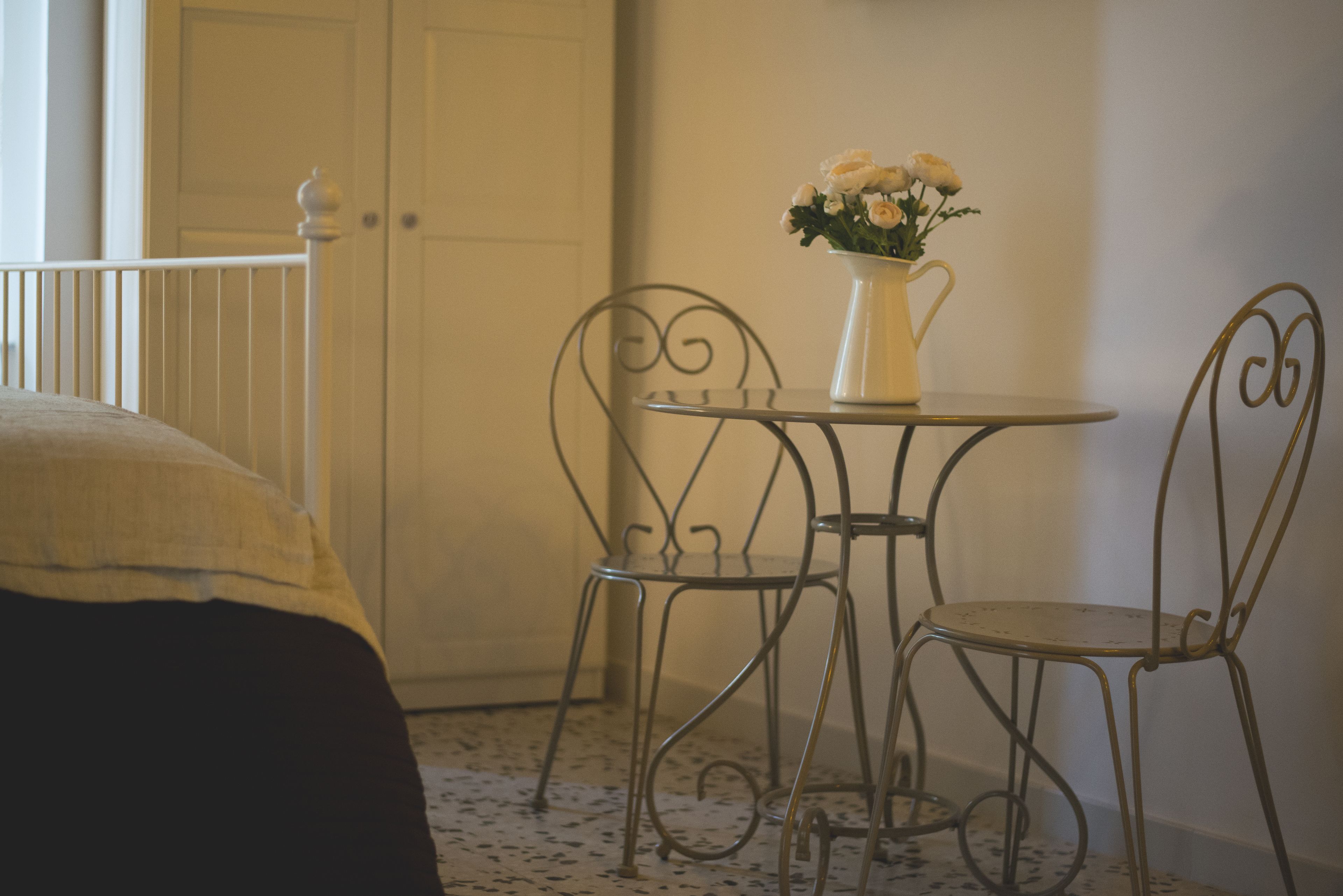 Una habitación pequeña con una cama, una mesa con un jarrón de flores y dos sillas.