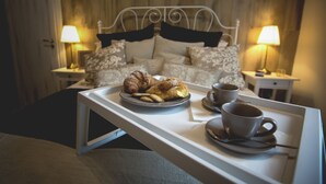A neatly made breakfast tray with croissants and coffee cups on a bed with a headboard, two bedside lamps, and a wooden wall in the background. - Elegant B&B Il Vicolo storico (Salerno)